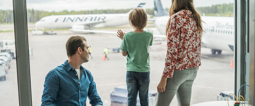 Family watching aeroplane from window in terminal.