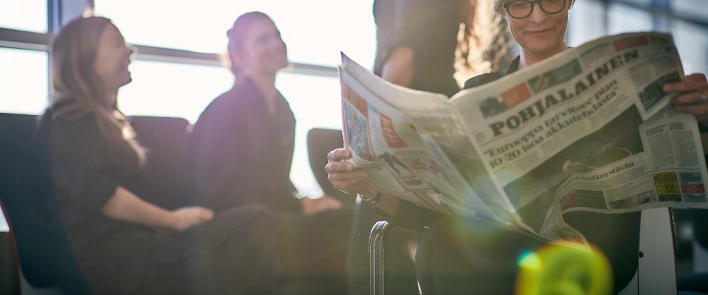 Passengers waiting for their flight. One is reading a newspaper.